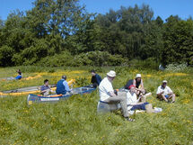 People sitting next to canoes in the grass. Photo. 
